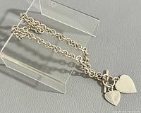 Silver necklace displayed on clear stand, showing chain and heart pendants.