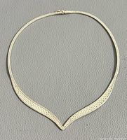 Silver chevron necklace laid flat on a gray textured surface, showing the overall shape and clasp.