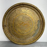 Full view of the round brass tray showing central figure and floral engravings with patina and minor wear on the edge.