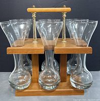 Front view of six ale glasses in the wooden stand with metal handle.