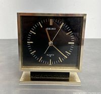 Front view showing the black dial with gold markers and hands, displaying time and Seiko branding.