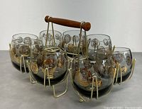 Front angle of eight glasses inside gold-toned metal carrier with wooden handle.