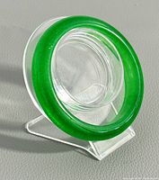 Green jade bangle displayed on clear stand showing round polished surface and vibrant color.