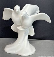 White porcelain figurine of two doves in flight on abstract base photographed from front angle against dark background.
