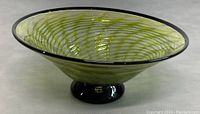 Side view of signed green swirled art glass footed bowl with black foot base