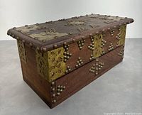 Oblique side view of the vintage wooden chest showing brass decorations and wood grain.