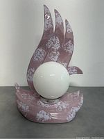 Front view of vintage Italian ceramic flame lamp with white spherical light central globe on pink flame-shaped base with white patches.