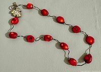Full view of the necklace laid out showing the red coral beads and silver leaf clasp.