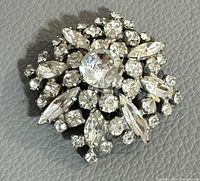 Top down image of the vintage brooch showing clear rhinestones of various shapes set in a silver-tone metal base.