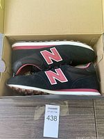 Pair of black and red New Balance shoes inside original box, showing side profile with 'N' logo visible.