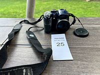 GE X500 digital camera with black neck strap and lens cap on wooden picnic table outdoors.