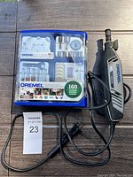 Dremel 300 rotary tool with power cord next to blue plastic accessory case containing 160 pieces of rotary tool bits and attachments