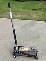 Side view of floor jack showing handle, wheels, and body with capacity label indicating 6000 lbs lifting capacity.