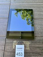 Front side of Apple iPad placed on a wooden surface showing screen with home button beneath it.