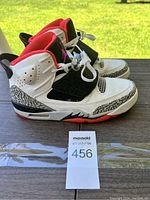 Side view of the left shoe showing white leather, black elephant print overlays, red lining and outsole