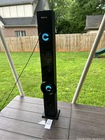 Full view of the tall black tower speaker on a table outdoors, showing the illuminated blue speaker ring and VIVITAR branding at the top.