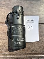 Top view of black monocular showing focus distance markings and 'day & night Field 22°' label, along with wrist strap attached.