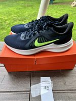 Side profile of the navy blue Nike running shoe showing neon green swoosh and white sole, placed on orange Nike shoebox.