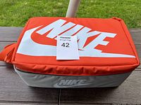 Closed orange and grey Nike carrying bag with large white Nike logo on the top.