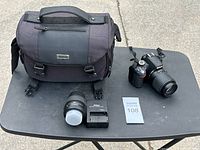Overall lot: camera body with lens attached, second lens, charger and Nikon case on table