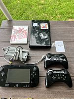 Full view of the Wii U console, GamePad, two Pro Controllers, power adapter, and Just Dance 3 game case on wooden table.