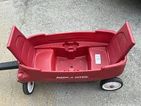 Front view of the red Radio Flyer wagon showing molded seating and cup holders, placed on concrete.
