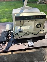 Full view of the Singer electric sewing machine with foot pedal, power adapter and hard plastic carrying case.