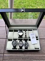 Full view of the open black watch box showing four wristwatches inside and one bracelet.