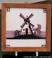 Front view of framed antique Delft tile with windmill hand-painted in purple hues on white ceramic with crackled surface.