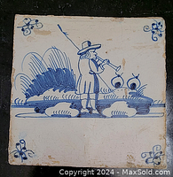 Full view of the antique square Delft tile showing the central painted figure of a musician playing a wind instrument with stylized nature elements in blue on white glaze.