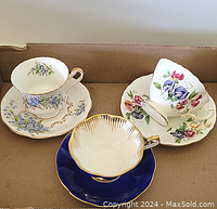 Three assorted teacups and saucers in a box showing different floral and gold trim patterns