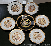Seven Japanese decorative plates with gold accents arranged in a pattern, showing their detailed artwork and gold trim.