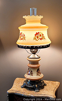 Full view of the vintage floral patterned glass table lamp lit up, showcasing the scalloped edge shade and clear glass chimney.