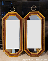 Pair of gilt wood framed elongated octagonal mirrors leaning against a dark background, showing front reflective surfaces and hanging rings.