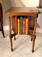 Wooden revolving bookcase end table with central rotating storage filled with books, viewed from front.