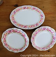 Full view of the set including one oval platter and two scalloped bowls decorated with pink, red, and yellow floral design and gold accents on a white background.