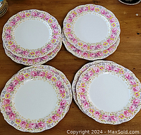Top view of 8 stacked Royal Albert Serena dinner plates showing floral rim pattern in pink, yellow, and blue with gold accents.