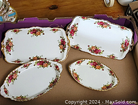 Four Royal Albert Old Country Roses porcelain serving trays displayed in a storage box, showing rectangular and oval shapes with floral designs, gold trim and cut-out handles.