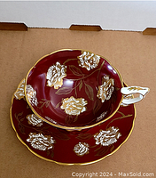 Teacup placed inside the matching saucer showing the burgundy color with gold flower pattern on the inside and top of the cup.
