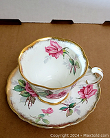 Front view of teacup on saucer showing pink rose floral pattern and gold rim.