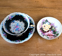 Top view of the teacup inside saucer showing floral patterns on black and white scalloped edges with gold accents, and the separate floral bowl with painted flowers.