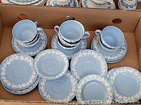 Box containing pale blue Wedgwood Queens Ware tea cups and saucers with white relief leaf decoration.