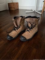 Pair of tan steel toe work boots with black accents shown on wood floor