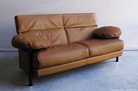 Front three-quarter view of sofa showing leather cushions and metal frame with glass side tables