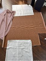 Four fabric pieces displayed on floor: caramel faux leather, off white linen, off white polyester curtain panel, checkered polyester fabric.