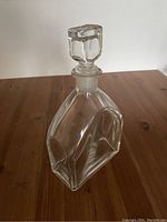 Front and side views of clear glass decanter with faceted geometric design and square glass stopper on wooden surface.