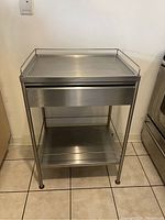 Front view of the stainless steel utility cabinet with drawer and open bottom shelf visible.