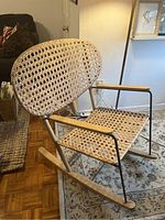 Side and front view of cane rocking chair showing woven cane seat and back, wooden armrests, metal frame and wooden rockers.