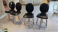 Four black vinyl and metal bar stools with round backrests and footrests arranged in a row on tiled floor.