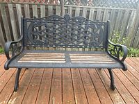 Front view of black cast aluminum bench with lattice backrest and wooden seat slats showing weathering.